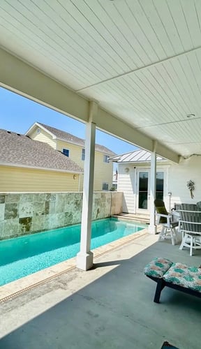 Covered patio with turquoise pool, lounge chairs, and Adirondack seating overlooking residential neighborhood