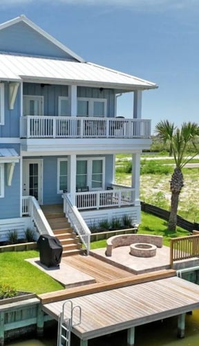 Blue and white elevated beach house with metal roof, wraparound decks, fire pit, and wooden dock on waterfront property