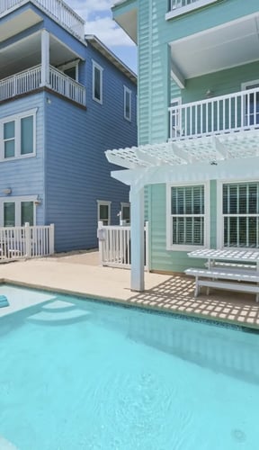 Backyard pool area with turquoise water, lounge chairs, and colorful beach houses with decks and railings